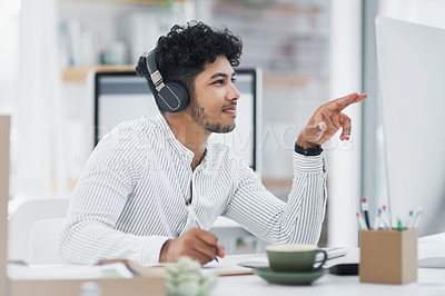 Buy stock photo Shot of a young businessman writing notes while working on a computer in an office