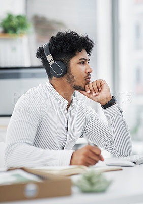 Buy stock photo Shot of a young businessman writing notes while working on a computer in an office