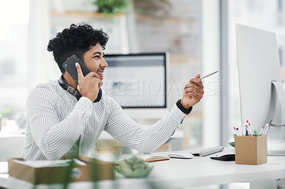 Buy stock photo Shot of a young businessman talking on a cellphone while working on a computer in an office