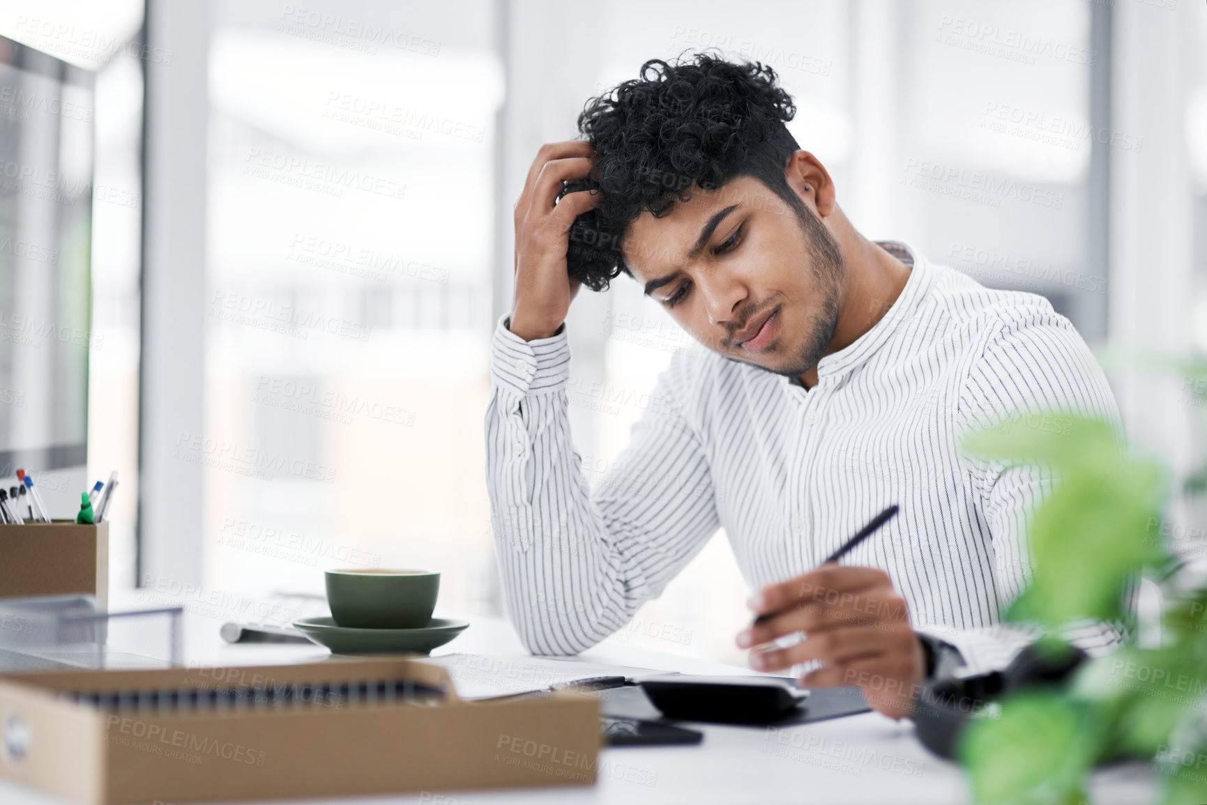 Buy stock photo Shot of a young businessman looking stressed out while using a calculator in an office