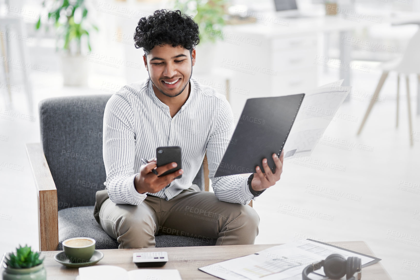 Buy stock photo Shot of a young businessman using a cellphone while going through paperwork in an office