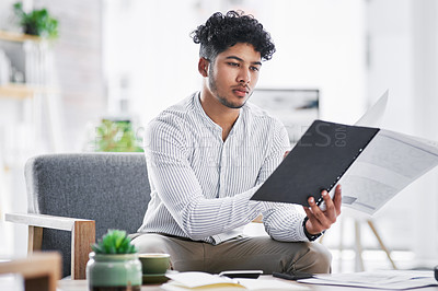 Buy stock photo Shot of a young businessman going through paperwork in an office