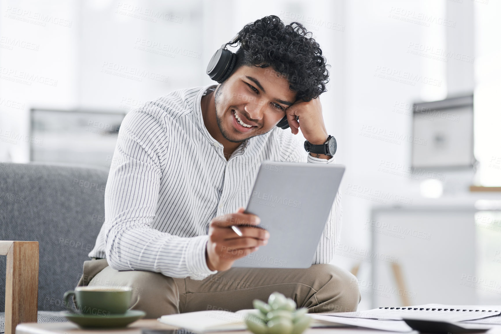 Buy stock photo Shot of a young businessman wearing headphones while using a digital tablet in an office