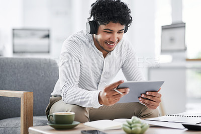 Buy stock photo Shot of a young businessman wearing headphones while using a digital tablet in an office