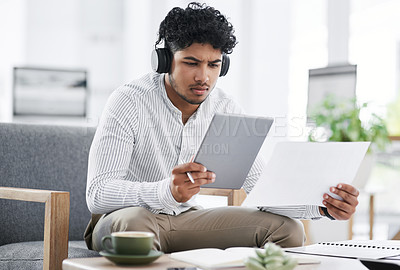 Buy stock photo Shot of a young businessman using a digital tablet while going through paperwork in an office