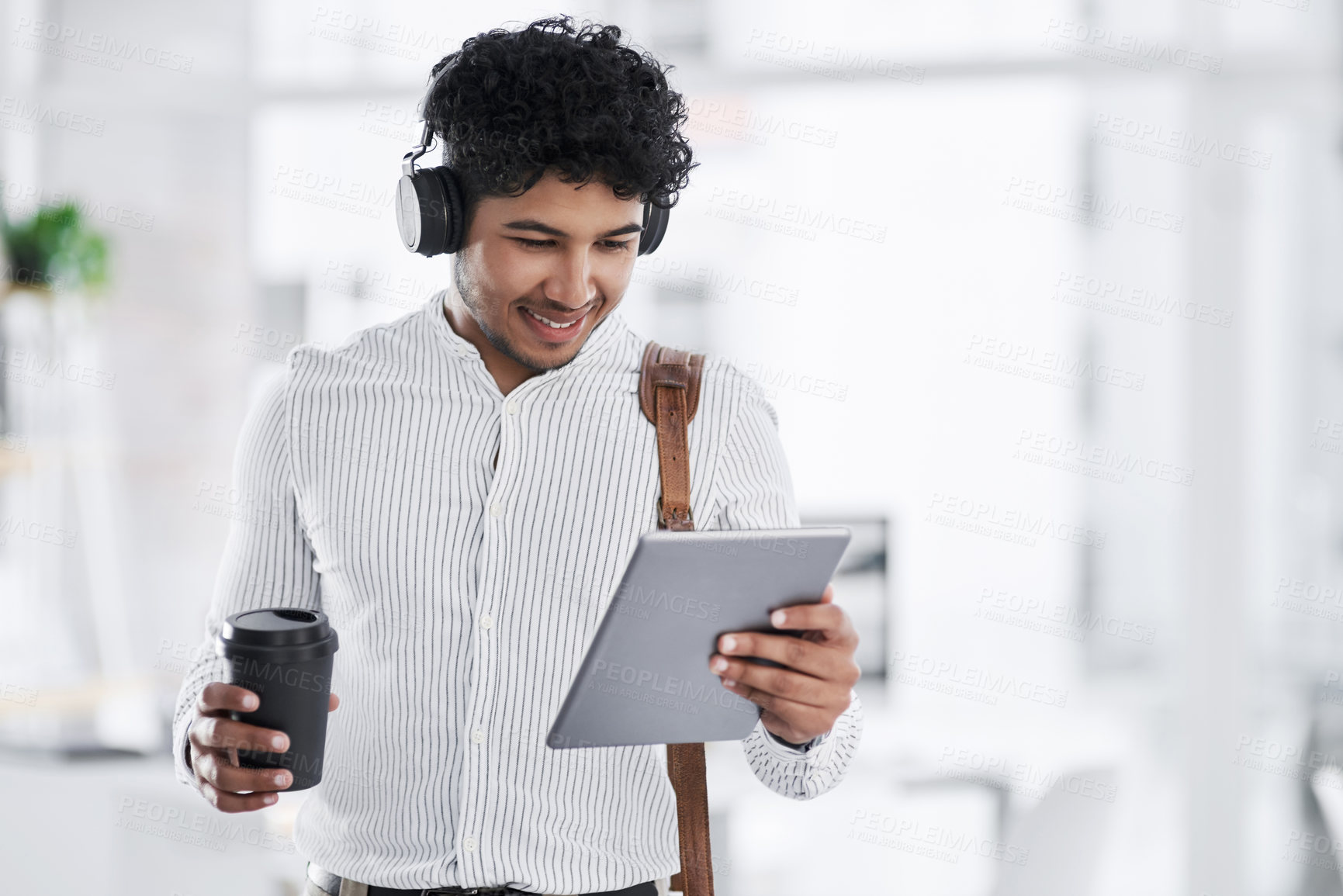 Buy stock photo Shot of a young businessman wearing headphones while using a digital tablet in an office