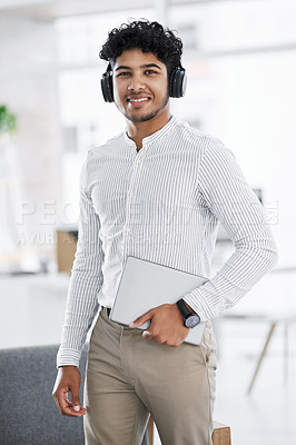 Buy stock photo Portrait of a young businessman wearing headphones and holding a laptop in an office