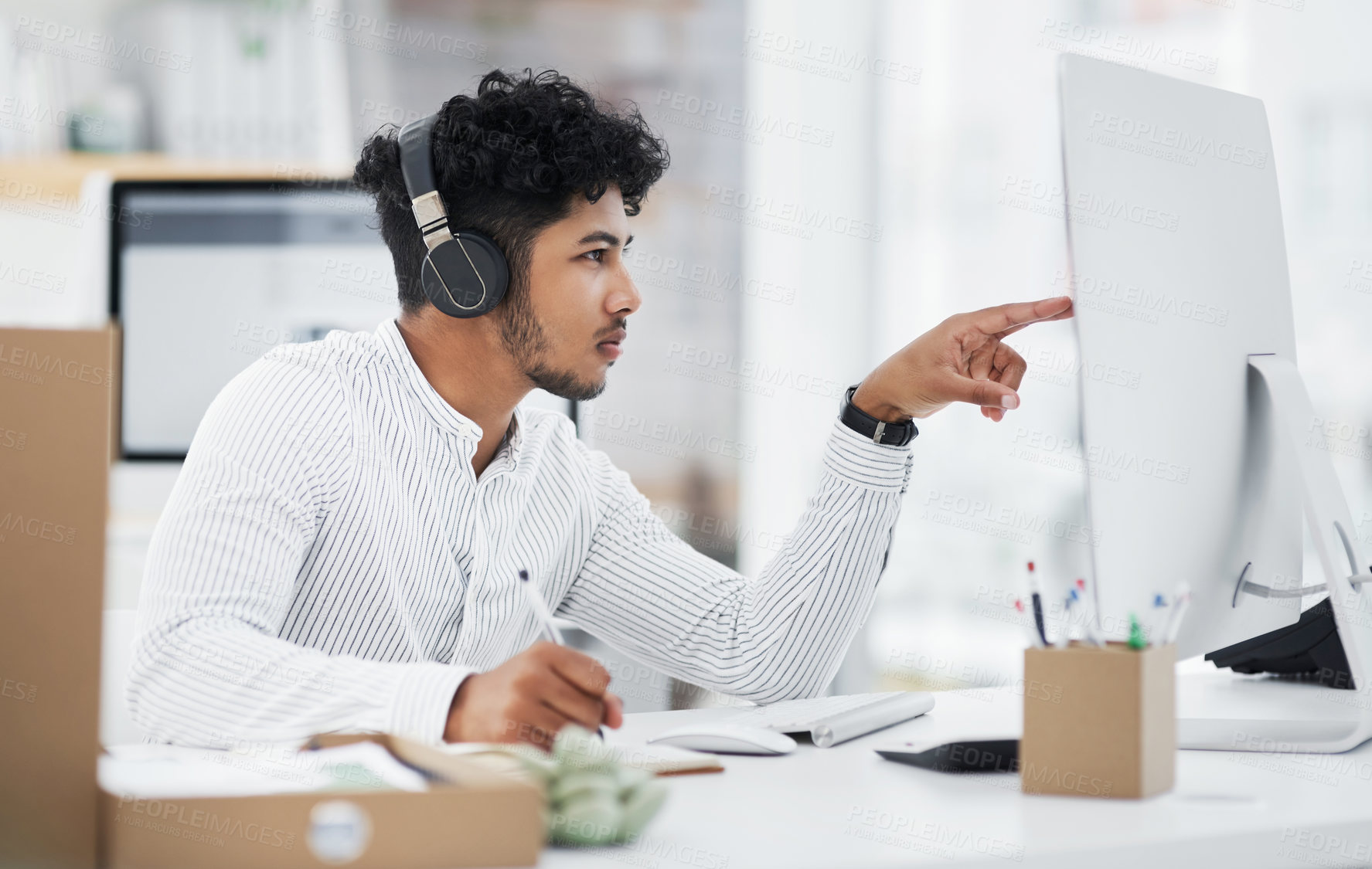 Buy stock photo Shot of a young businessman wearing headphones while working on a computer in an office