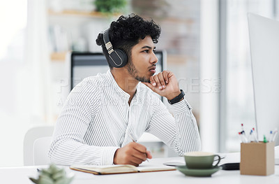 Buy stock photo Shot of a young businessman looking thoughtful while working on a computer in an office