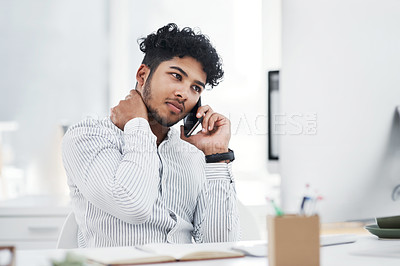 Buy stock photo Shot of a young businessman looking stressed out while talking on a cellphone in an office