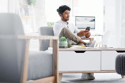 Buy stock photo Shot of a young businessman using a cellphone in an office