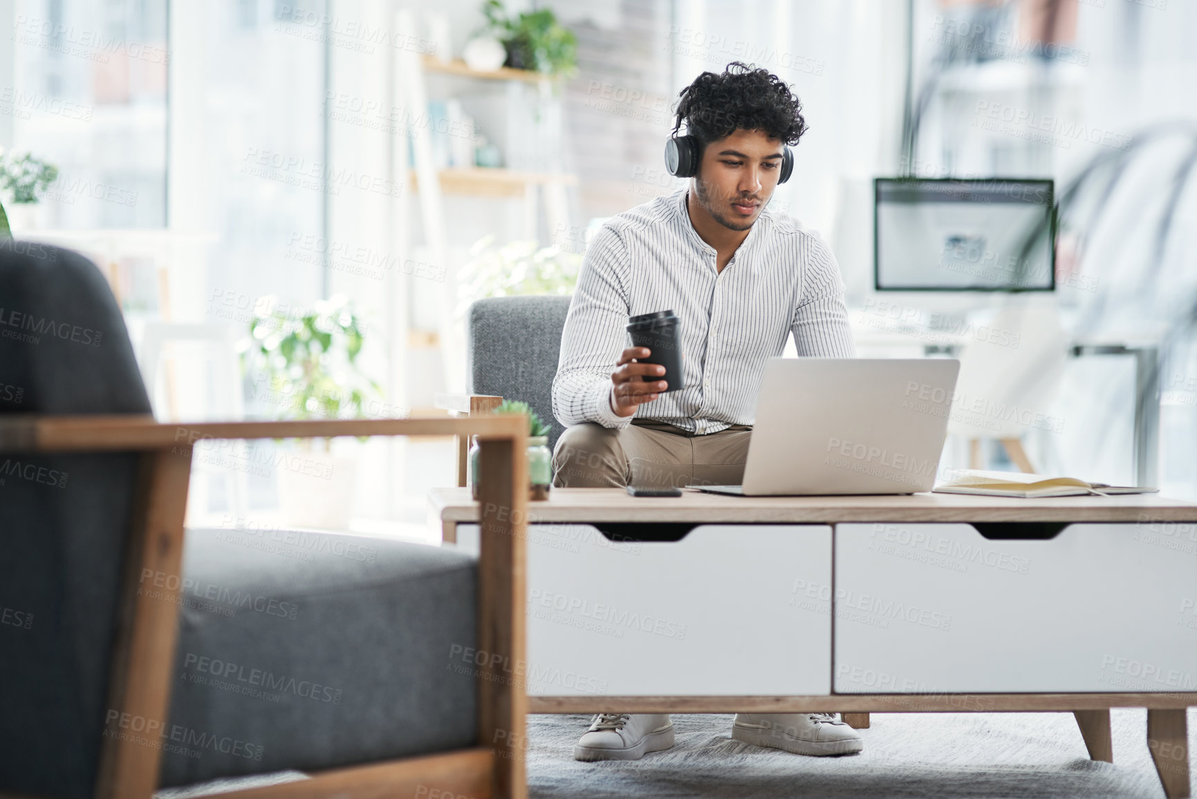 Buy stock photo Shot of a young businessman wearing headphones while working on a laptop in an office