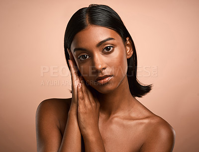Buy stock photo Portrait of a beautiful young woman touching her face while posing against a brown background