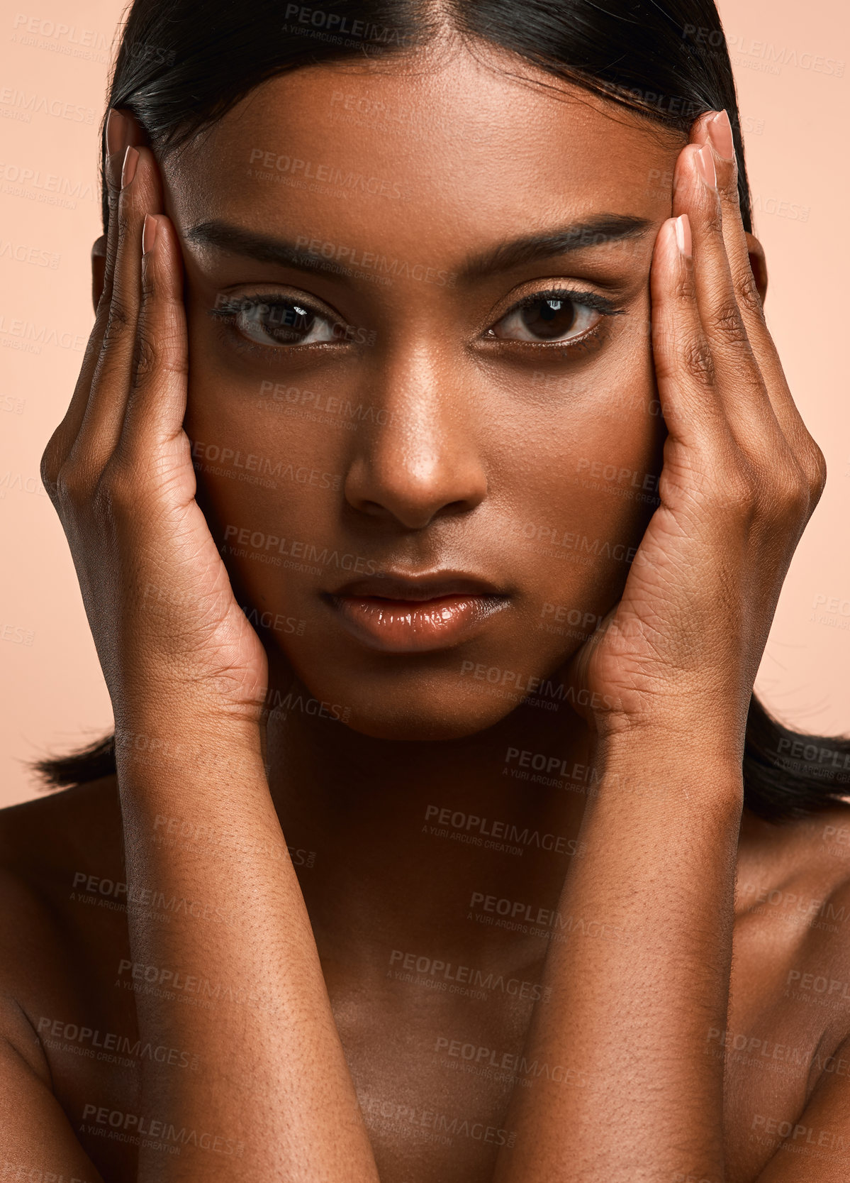 Buy stock photo Portrait of a beautiful young woman touching her face while posing against a brown background