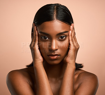 Buy stock photo Portrait of a beautiful young woman touching her face while posing against a brown background