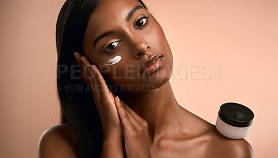 Buy stock photo Portrait of an attractive young woman applying moisturiser against a brown background