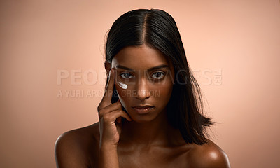 Buy stock photo Portrait of an attractive young woman applying moisturiser against a brown background