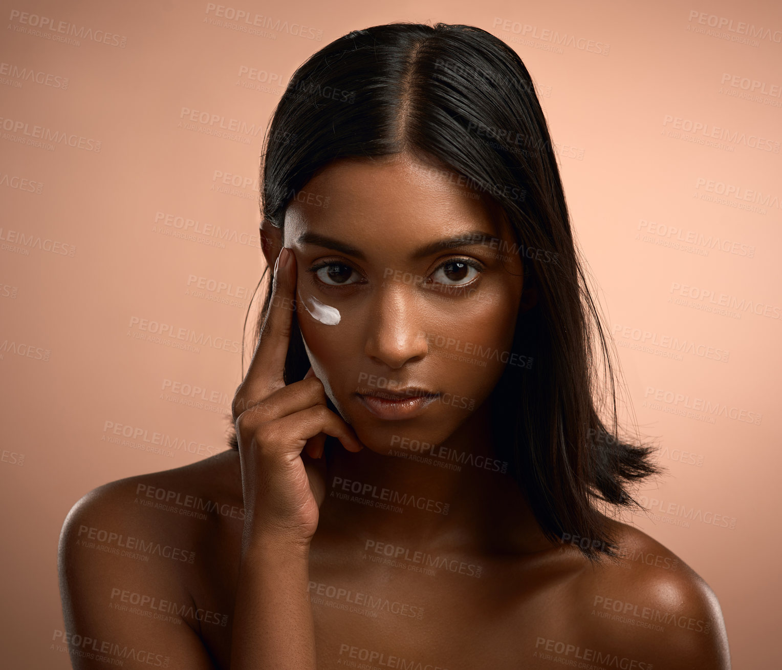 Buy stock photo Portrait of an attractive young woman applying moisturiser against a brown background