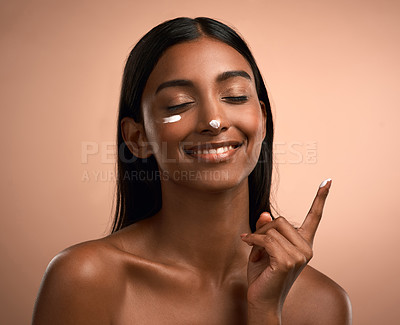 Buy stock photo Shot of an attractive young woman applying moisturiser against a brown background