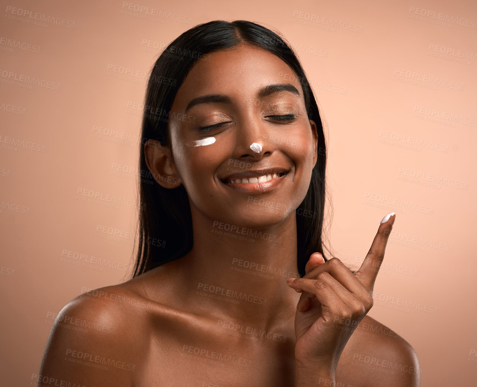 Buy stock photo Shot of an attractive young woman applying moisturiser against a brown background