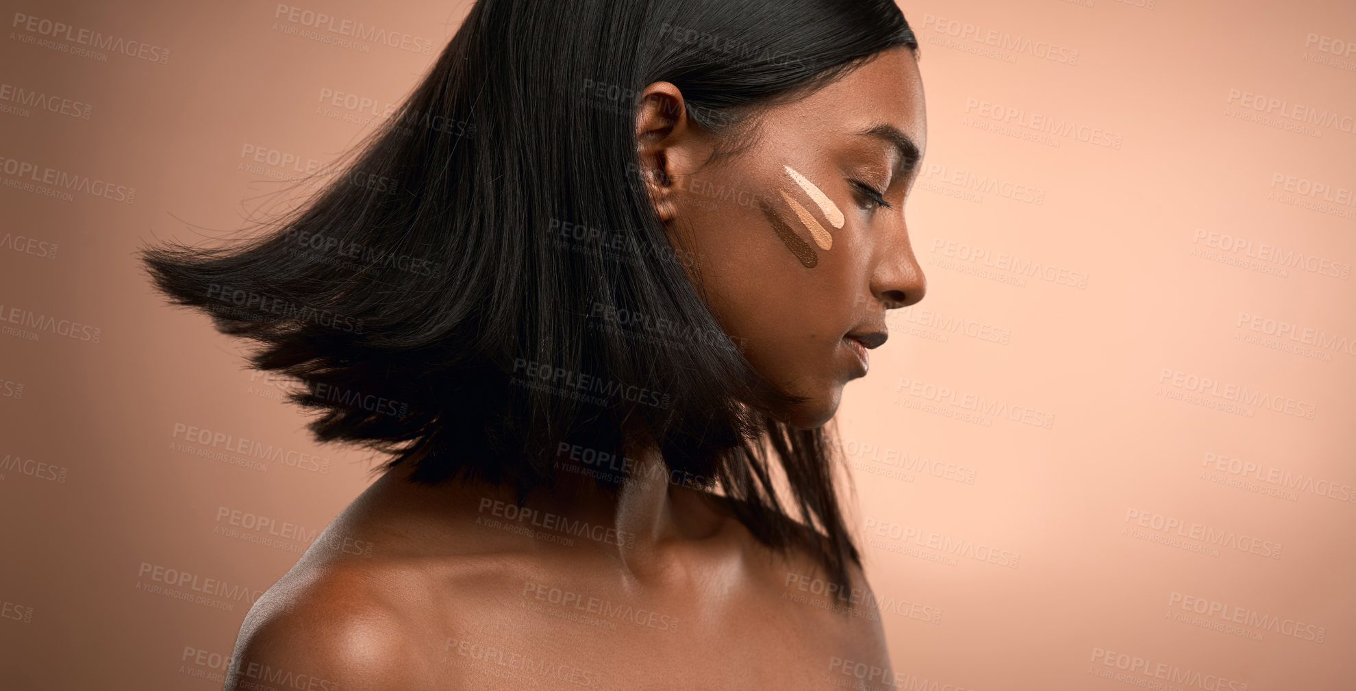 Buy stock photo Shot of an attractive young woman applying foundation to her face against a brown background