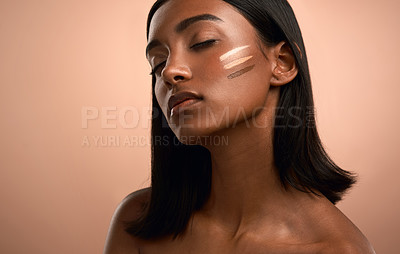 Buy stock photo Shot of an attractive young woman applying foundation to her face against a brown background
