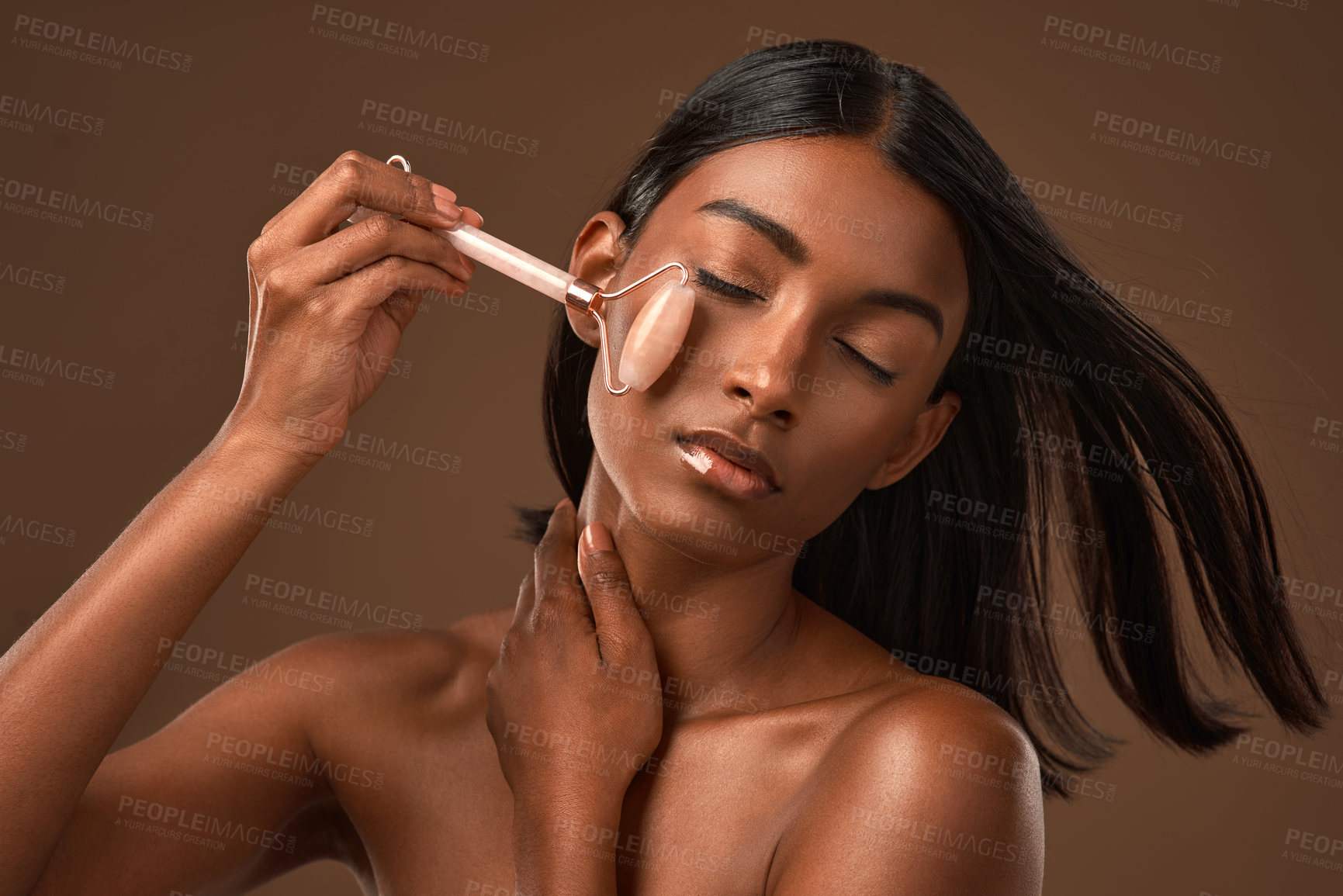 Buy stock photo Shot of an attractive young woman using a derma roller against a brown background