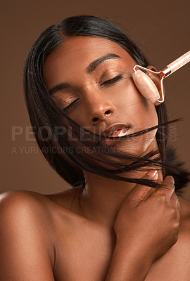 Buy stock photo Shot of an attractive young woman using a derma roller against a brown background