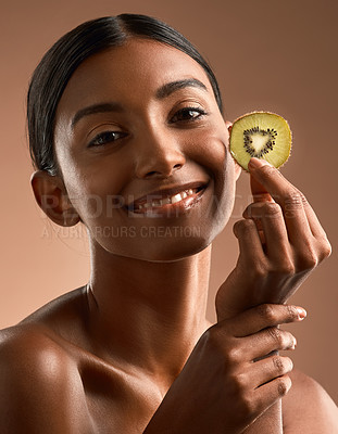 Buy stock photo Portrait of a beautiful young woman posing with a slice of kiwi fruit against a brown background