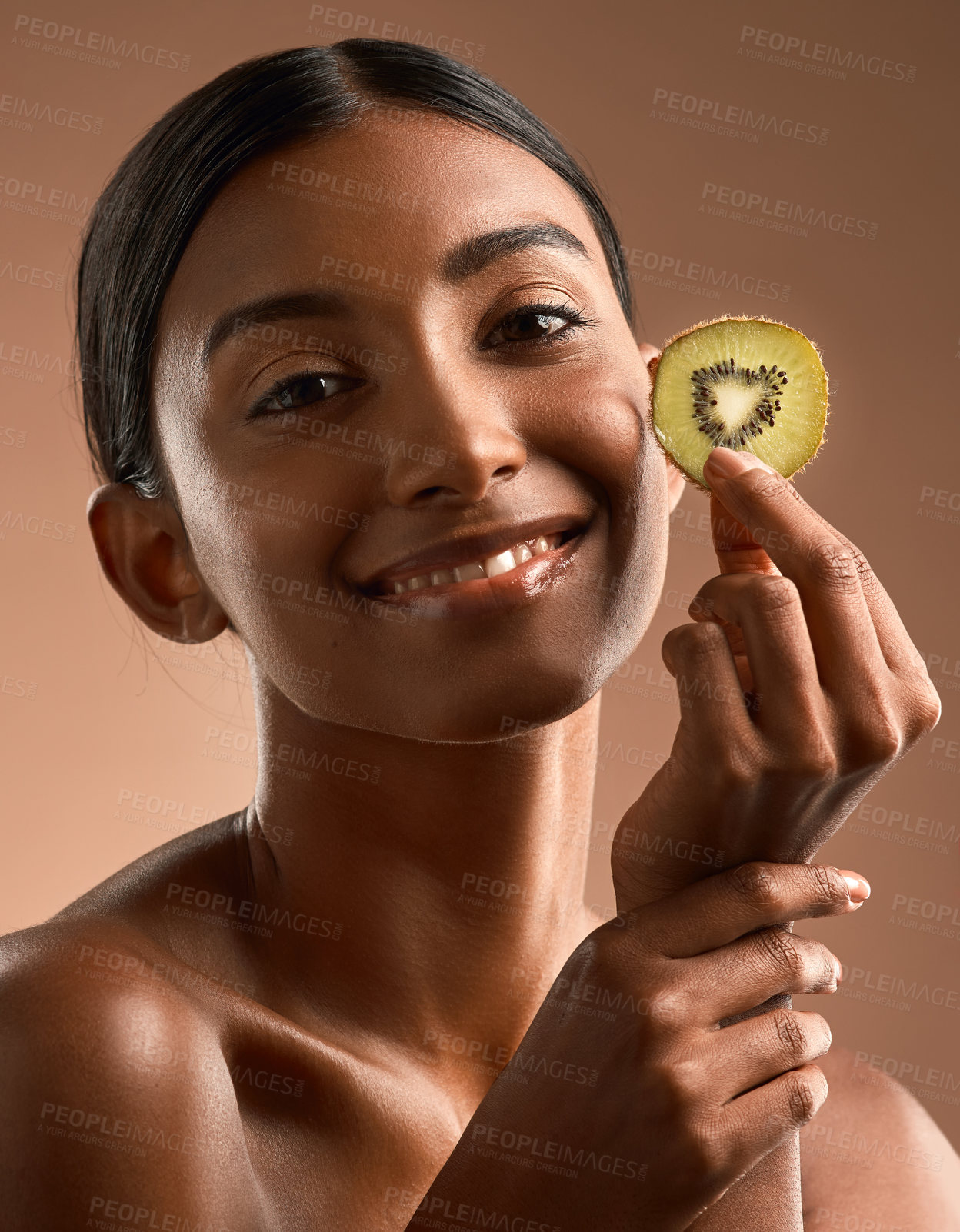 Buy stock photo Portrait of a beautiful young woman posing with a slice of kiwi fruit against a brown background