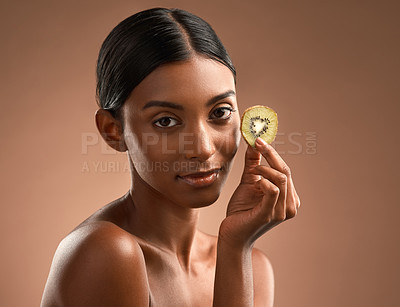 Buy stock photo Portrait of a beautiful young woman posing with a slice of kiwi fruit against a brown background