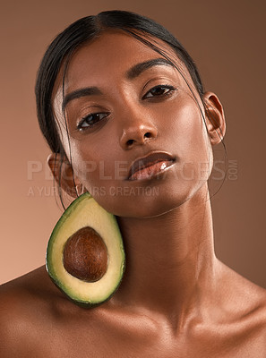 Buy stock photo Portrait of a beautiful young woman posing with an avocado  against a brown background