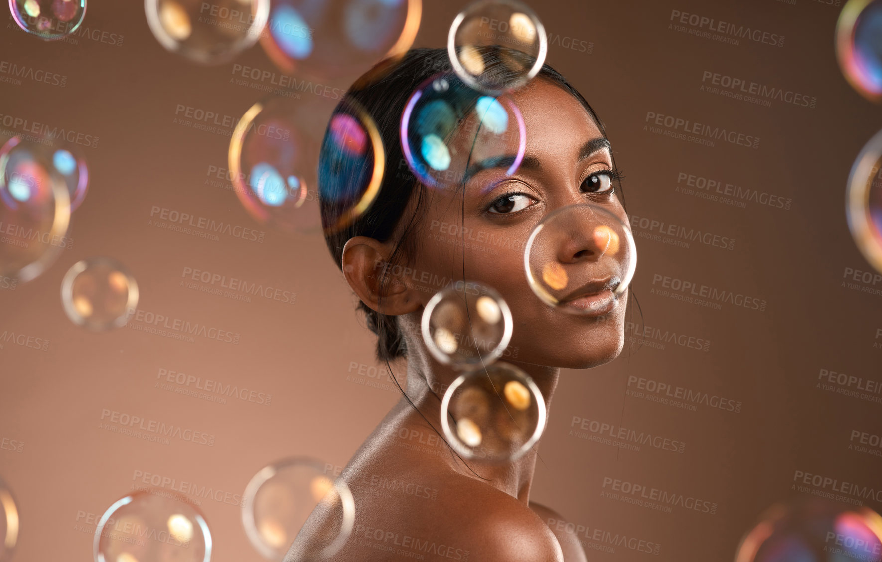 Buy stock photo Portrait of a young attractive woman posing with bubbles against a brown background