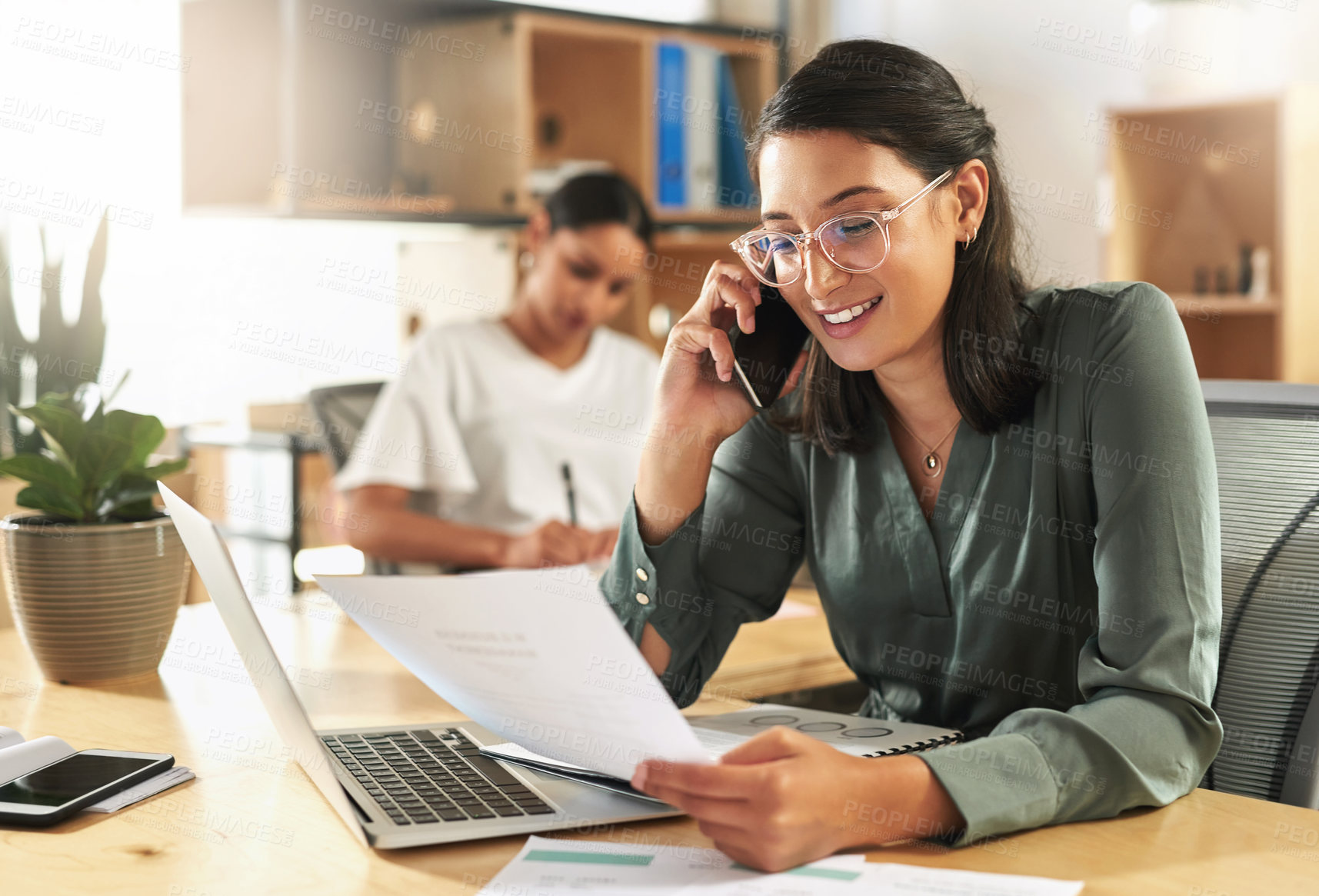 Buy stock photo Shot of a young businesswoman reading paperwork while using her smartphone