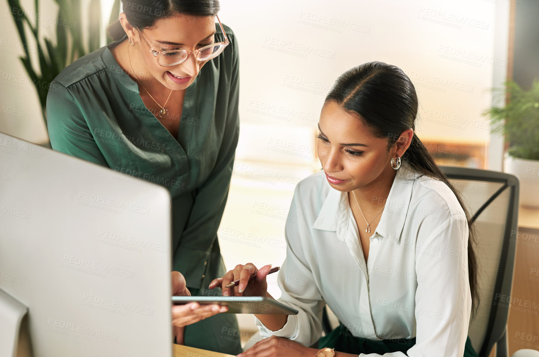 Buy stock photo Shot of two businesswomen using a digital tablet to oversee work