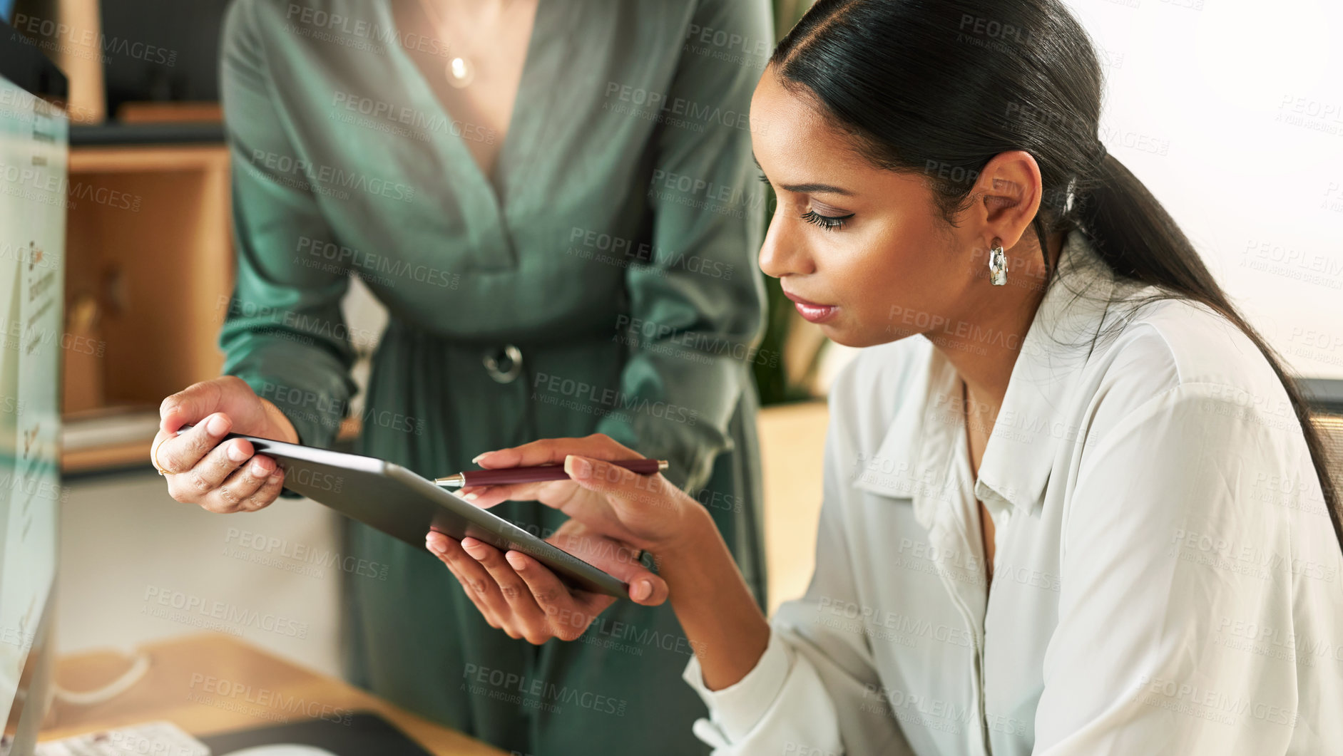 Buy stock photo Shot of two businesswomen using a digital tablet to oversee work