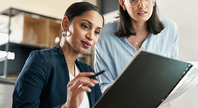 Buy stock photo Shot of two female coworkers surveying paperwork