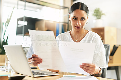 Buy stock photo Shot of a young businesswoman reviewing paperwork at work