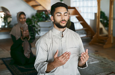 Buy stock photo Shot of a young muslim couple praying in the lounge at home
