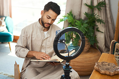 Buy stock photo Shot of a young muslim man reading while doing his vlogg in the lounge at home