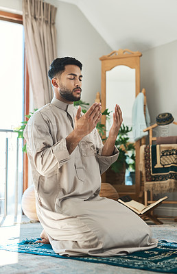 Buy stock photo Shot of a young muslim man praying in the lounge at home