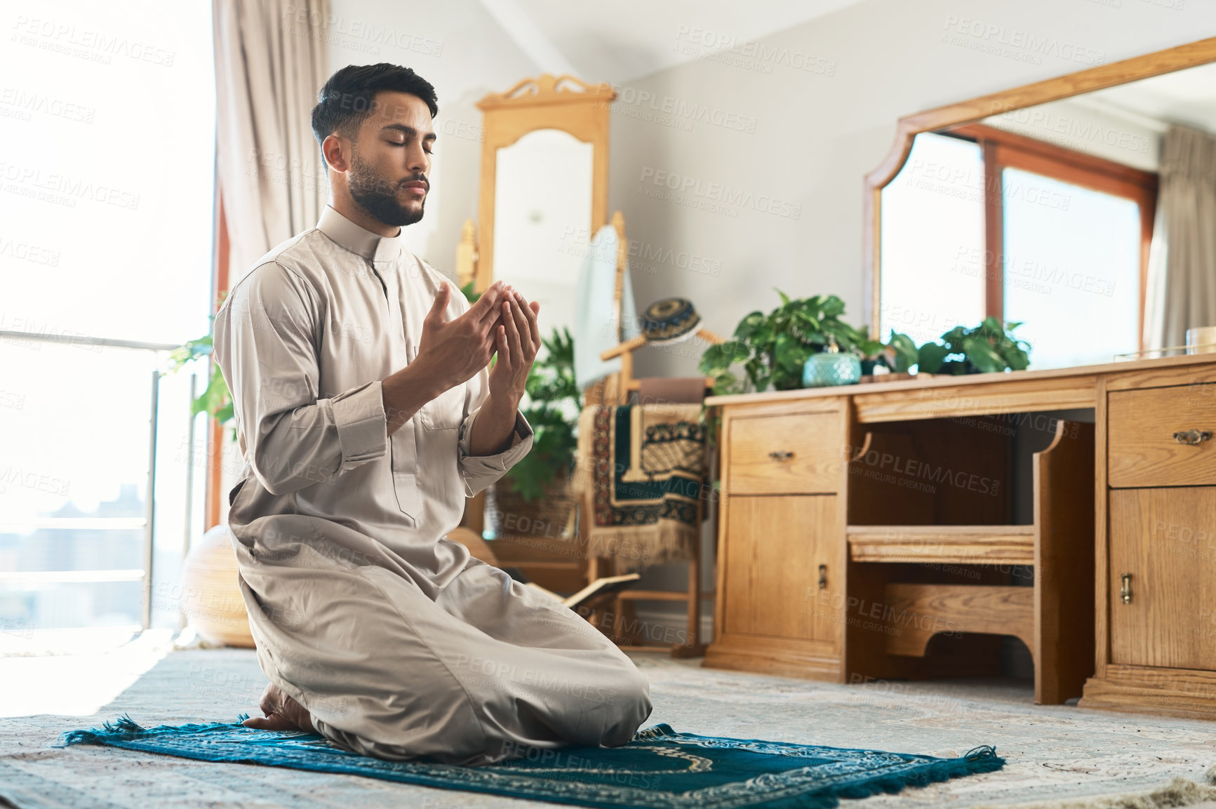 Buy stock photo Shot of a young muslim man praying in the lounge at home