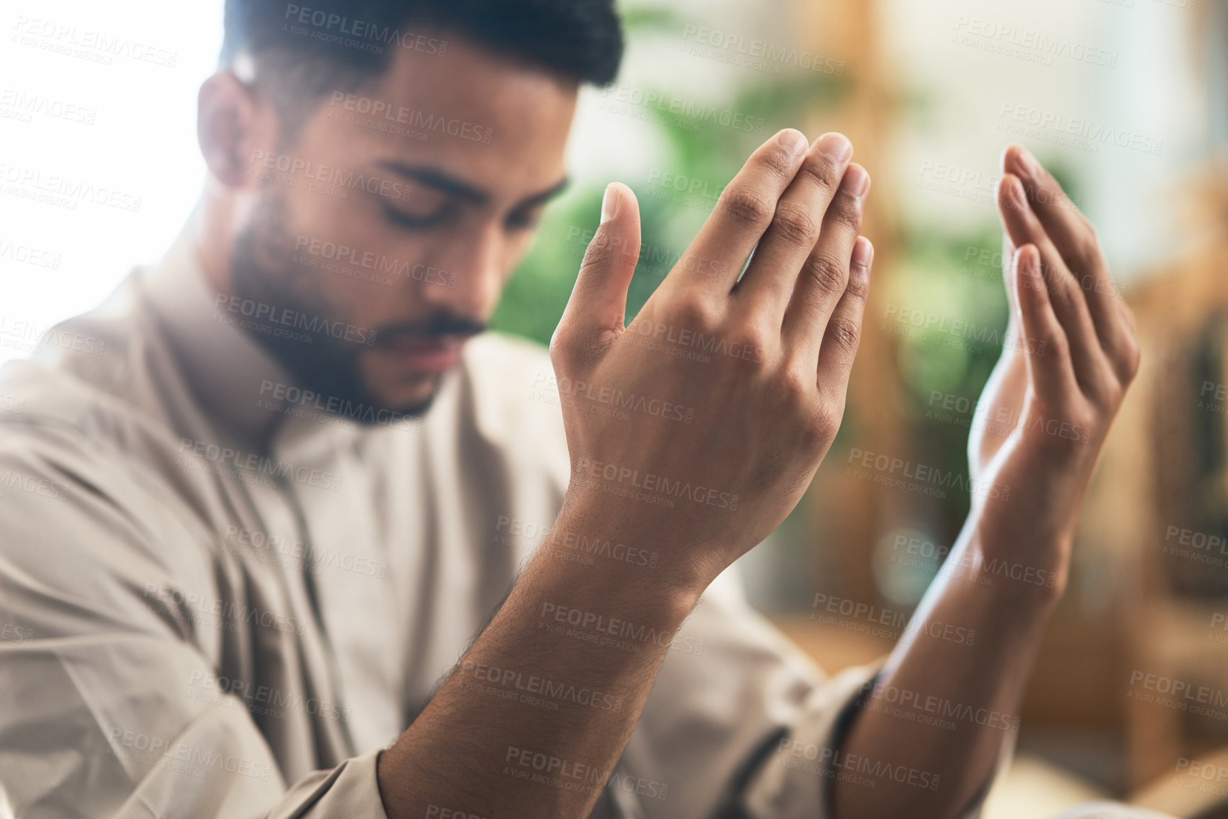 Buy stock photo Shot of a young muslim man praying in the lounge at home
