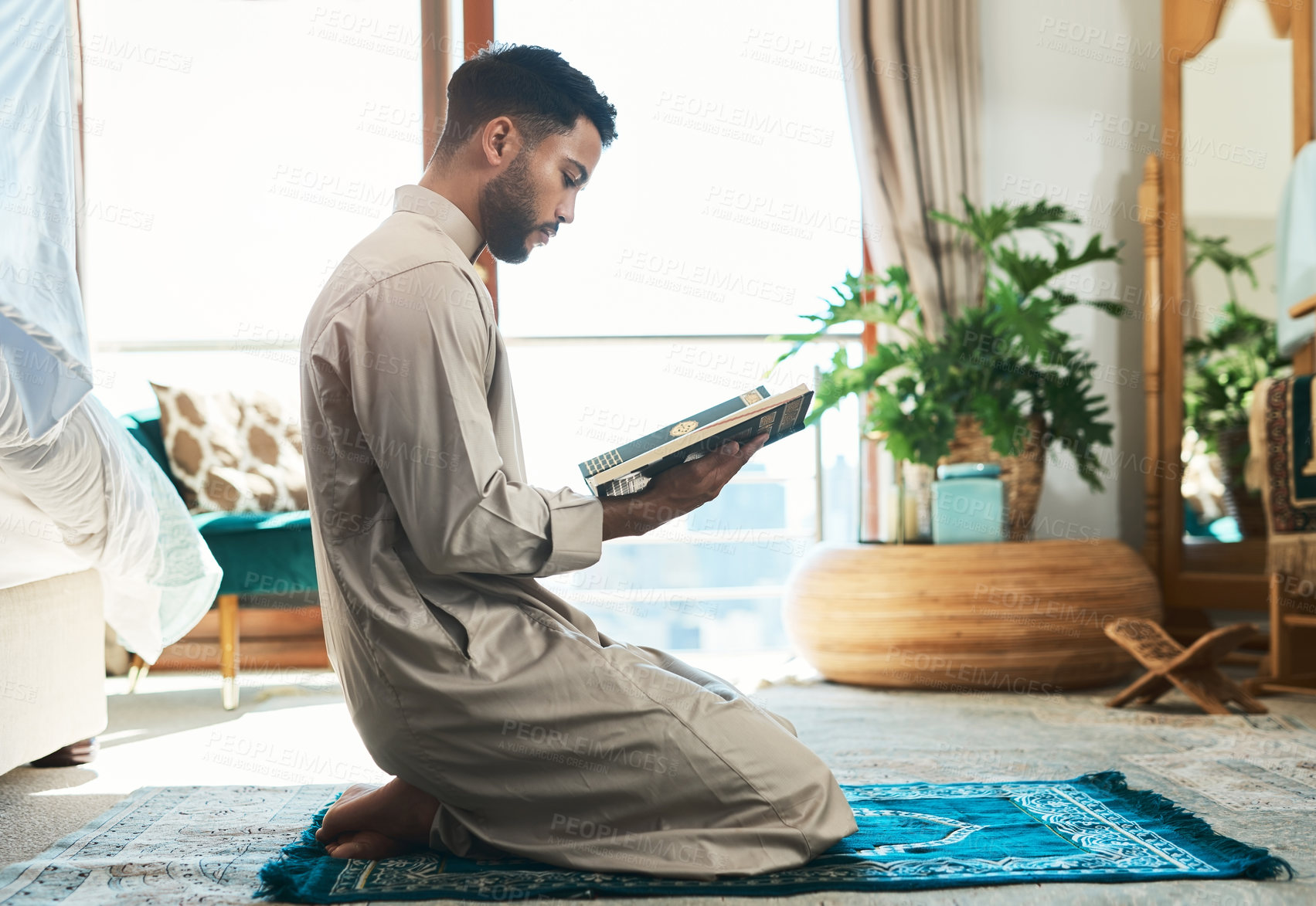 Buy stock photo Shot of a young muslim man reading in the lounge at home