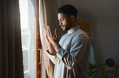 Buy stock photo Shot of a young muslim man praying in the lounge at home