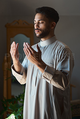 Buy stock photo Shot of a young muslim man praying in the lounge at home