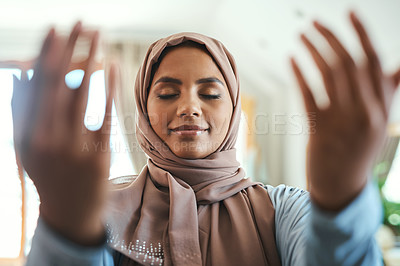 Buy stock photo Shot of a young muslim woman praying in the lounge at home