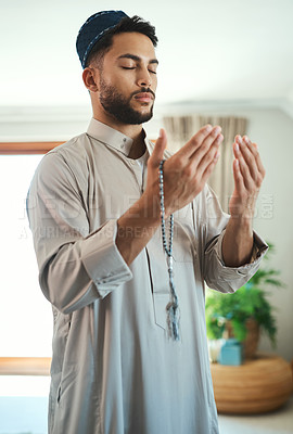 Buy stock photo Shot of a young muslim man praying in the lounge at home