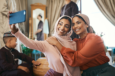 Buy stock photo Muslim sisters taking selfies in traditional Islamic head scarf inside a happy family home together. Beautiful young women who are proud of their religion post photos of Eid Ramadan on social media