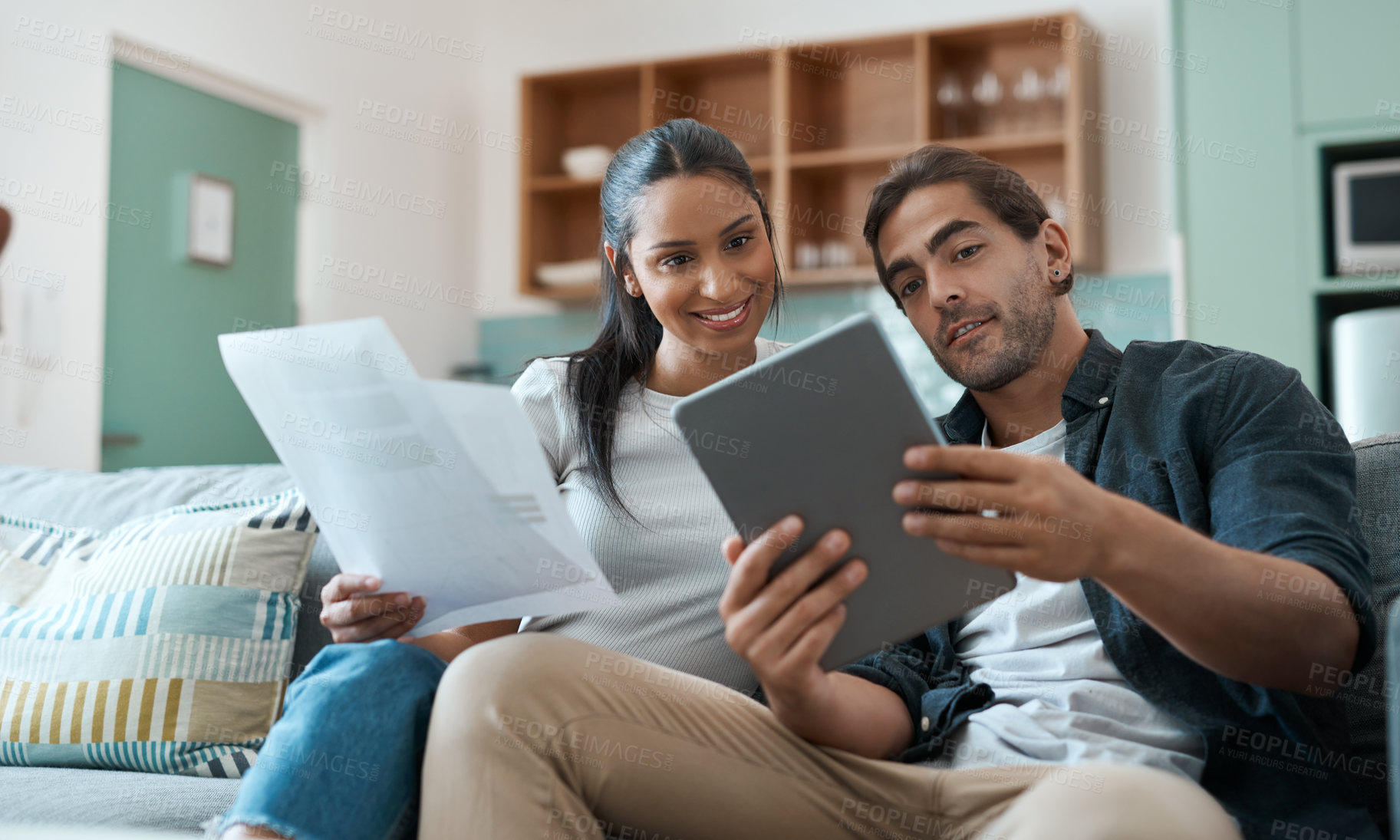 Buy stock photo Shot of a young couple doing paperwork while using a digital tablet at home